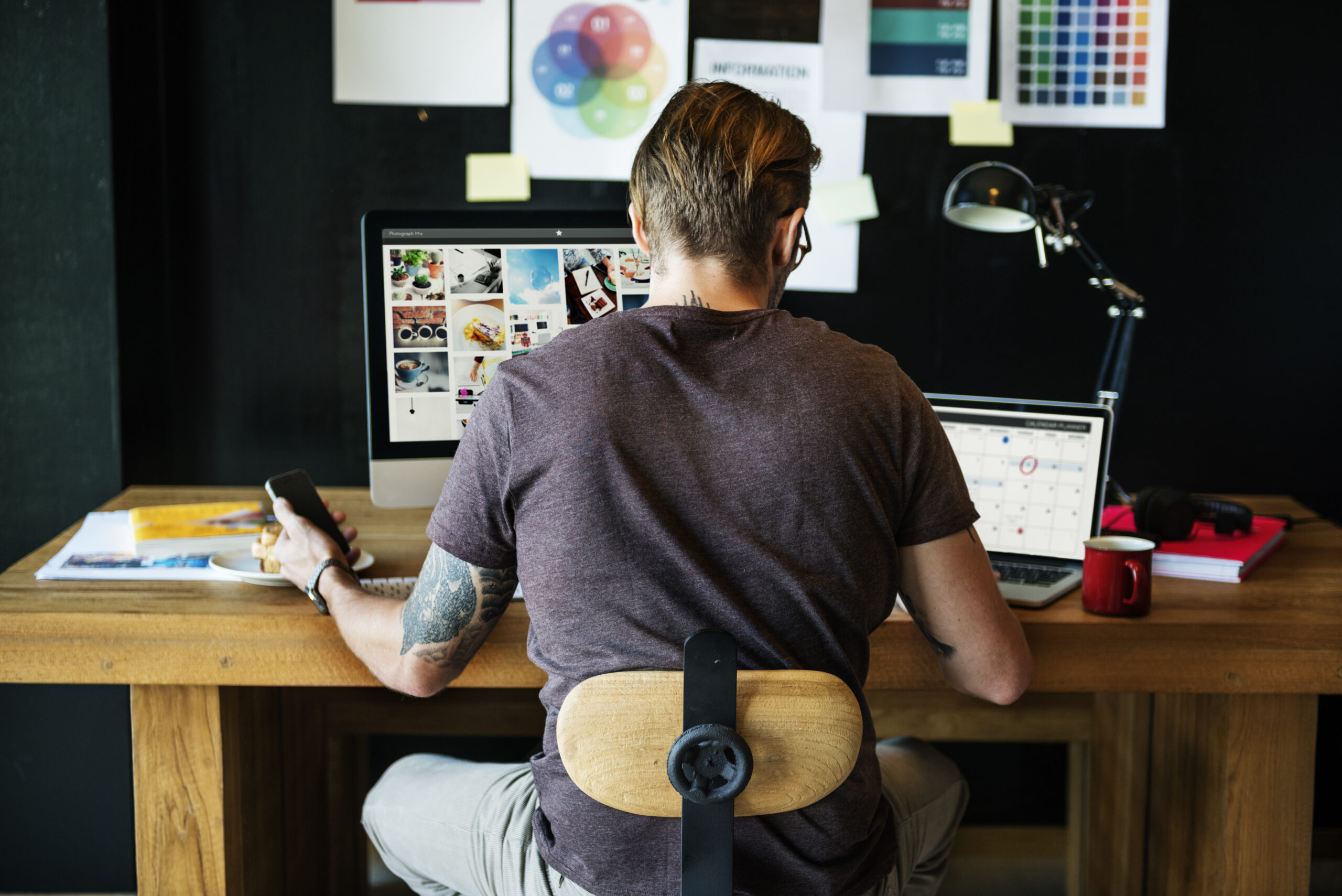 Workspace - Arbeitsbereich mit Laptop, Mac, Stuhl und Person mit mobilem Telefon